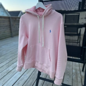 Ljusrosa hoodie från Polo Ralph Lauren - Säljer en ljusrosa hoodie från Polo Ralph Lauren med vit dragsko och klassisk känguruficka. Tröjan har en broderad blå logga på bröstet och är perfekt för en avslappnad stil. Supermjuk och skön med huva. Nypris 2299kr