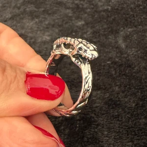 Fantasyinspirerad drakring i rostfritt stål med skulpterade detaljer - Detaljerad ring i rostfritt stål med kraftfullt drakhuvud och snidade fjäll längs bandet. Innerdiameter ca 2 cm, höjd ca 0,7 cm. I nyskick – stilren men uttrycksfull design med fantasyattityd. Ingen prutning, men bundlerabatt erbjuds vid köp av flera varor.  