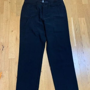 Svarta kostymbyxor från Peppercorn - Stilrena svarta kostymbyxor från Peppercorn med raka ben och hög midja. Byxorna har diskreta framfickor och en bakficka med knapp. Perfekta för en dressad look.