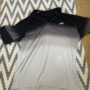 Svart och grå pikétröja med hästlogga - Säljer en snygg pikétröja i svart och grått med diskret horisontellt mönster och broderad vit hästlogga på bröstet. Tröjan har korta ärmar och klassisk krage med knappar. Perfekt för dig som gillar stilren design.