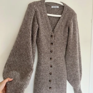 Adoore Montana klänning  - Superfin grå långklänning från Adoore i ribbstickat material. Klänningen har v-ringning, långa puffärmar och knappar hela vägen framtill. Köpt för ca en månad sedan, men använd fåtal gånger. Fortfarande i skick som ny!