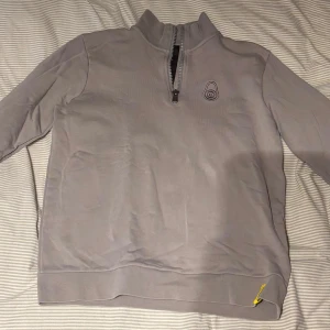 Ljusgrå sail racing halvzip tröja med broderad logga - Ljusgrå tröja med halv dragkedja och hög krage. Broderad logga på bröstet och liten gul detalj vid nederkanten. Mjuk och bekväm, perfekt för lager-på-lager. Långärmad modell. Sail racing, ny skick. Använt 2-5 gånger. Är S men sitter som S-M.