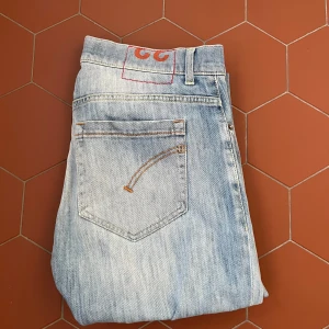 Ljusblå Dondup jeans - Säljer ett par ljusblå jeans från Dondup med raka ben och klassisk femficksdesign. Jeansen har orangea sömmar och en diskret logga bak i midjan. Perfekta för en avslappnad stil och passar till det mesta. Pris kan diskuteras! 😎