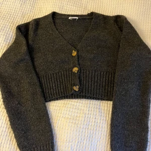 Mörkgrå croppad kofta med knappar - Mörkgrå croppad stickad kofta från Vero Moda. Använd mycket men fortfarande bra skick. Lapparna är bortklippa men storlek Xs eller S. 