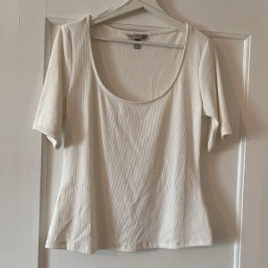 Vit ribbad topp från H&M - Säljer en vit ribbad topp från H&M med korta ärmar och rund, djup ringning. Toppen är i stretchigt material och har en enkel, stilren design som passar till många olika outfits.