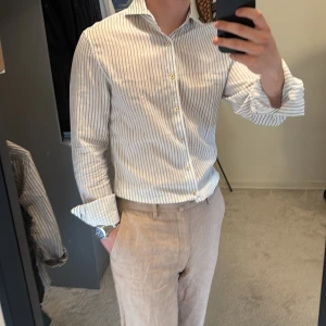 Vit och blå randig skjorta från Stenströms - Säljer en klassisk vit skjorta med tunna blå ränder från Stenströms. Skjortan har lång ärm, knappar framtill och en snygg krage. Perfekt för en stilren look och tillverkad i mjuk bomull och linne.