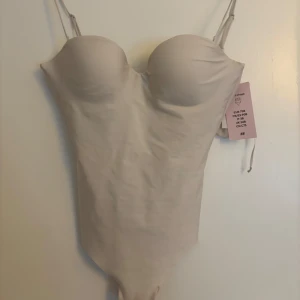 Vit body från H&M - Säljer en stilren body från H&M med vadderade kupor och tunna axelband. Bodyn har en enkel och elegant design som ger en smickrande siluett. Aldrig använd!💕