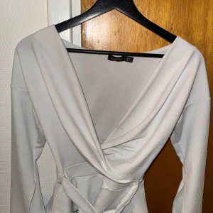 Vit omlottklänning  - Säljer en vit  blus  från boohoo med lång ärm och knytband i midjan. Blusen  har en djup v-ringning och är tillverkad i ett mjukt tyg som ger en elegant look.