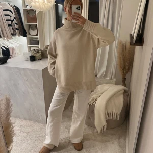 Beige stickad polotröja från H&M  - Säljer en oversized beige stickad polotröja med hög krage och långa ärmar. Tröjan har breda ribbade muddar vid ärmslut och nederkant, och är perfekt för lager-på-lager-stil. Enkel och stilren design som passar till mycket.