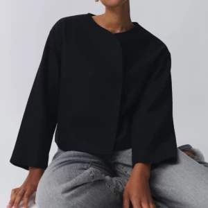 Svart Jacka  från Gina Tricot  - Elegant jacka från gina tricot med en minimalistisk design. Kavajen har en rund halsringning och en stilren, knapplös front. Perfekt för en stilren look.