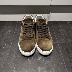 Bruna mocka sneakers med vit sula - Säljer ett par bruna sneakers i mocka med vita sulor och bruna skosnören. Skorna har en klassisk rund tå och platt sula, perfekt för en stilren vardagslook. Insidan är vit och de har en enkel, tidlös design.