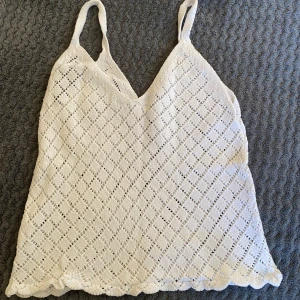 Vit virkad linnetopp från Sinsay - Superfin vit virkad linnetopp från Sinsay i storlek XXS. Toppen har tunna axelband, v-ringning och ett snyggt hålmönster i rutigt. Perfekt till sommaren och enkel att styla med jeans eller kjol!