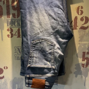 Blå jeans med bakficka och läderpatch - Klassiska blå jeans med en tydlig bakficka och läderpatch vid linningen. Jeansen har en normal passform och är perfekta för vardagsstilen. Storlek W31/L32 enligt etiketten.