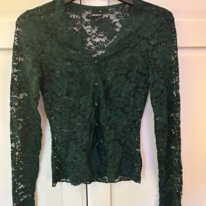 Grön spetsblus med knappar - Säljer en mörkgrön långärmad blus i spets från Gina Tricot. Blusen har lösa trådar, går att klippa bort! Men inte min stil. Storleken är xs och sitter tight.