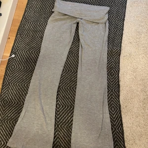 Grå mjukisbyxor från Gina Tricot - Grå mjukisbyxor från Gina Tricot med bred, vikt linning och utsvängda ben. Byxorna är tillverkade i mjukt bomullsmaterial och har en avslappnad passform som är perfekt för en chill stil.