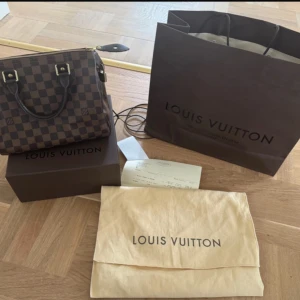 Louis Vuitton Speedy 25 Damier Ebene - Jättefin Louis Vuitton Speedy 25 Damier Ebene i jättefint skick. Finns någon liten fläck inuti på fodret. Knappt använd utan mest legat i sin dustbag.  Jag köpte väskan i Louis Vuitton-butiken i Stockholm 2010. Lås med nycklar, dustbag, presentbox och kasse samt originalkvitto medföljer.  Klassisk väska vars värde stiger med åren.   Kommer ifrån ett rökfritt hem. (Finns på fler sidor).