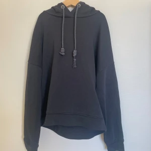 Svart hoodie från ONLY - En svart hoodie från ONLY med huva och dragsko. Tröjan har en avslappnad passform och är tillverkad i mjukt material, perfekt för vardagsbruk. Klassisk design utan tryck eller mönster.