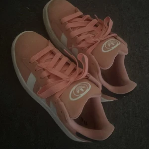 Campus 00s i rosa - Säljer ett par rosa campus 00s med vita detaljer och klassiska ränder på sidorna. Skorna har snörning och en beige sula med gummiyta undertill. Perfekta för dig som gillar sportig och stilren look. Använda 2 gånger.