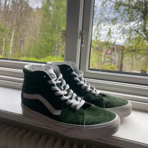 Gröna Vans Sk8-Hi sneakers - Säljer ett par gröna Vans Sk8-Hi sneakers med vit sula och vit sidostrip. Skorna har högt skaft, snörning och är gjorda i mocka. 