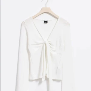Vit långärmad topp med knyt framtill - Säljer en vit långärmad topp med v-ringning och knyt framtill. Tunn och lätt i materialet, perfekt för lager-på-lager eller som en enkel statement-piece.