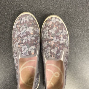 Blommiga skor - Säljer ett par skor med blommigt mönster i lila, grått och vitt. Skorna har rund tå och platt sula, perfekt för dig som gillar en avslappnad och färgglad stil. Storlek 36.