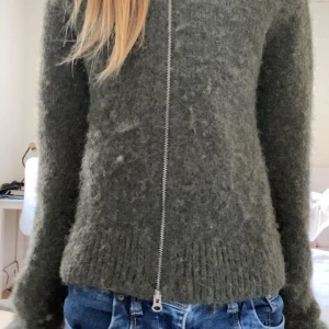 Mörkgrön stickad kofta med dragkedja - Mysig mörkgrön stickad kofta med lång ärm och dragkedja framtill. Koftan har en lite fluffig yta och ribbade muddar vid ärmslut och nederkant. Perfekt för lager-på-lager och enkel att matcha med jeans. NYPRIS ÄR 500 TROR JAG!!!