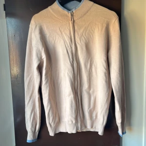 Beige kofta med dragkedja - Säljer en stilren beige kofta med dragkedja. Den har långa ärmar och en ribbad krage samt muddar. Perfekt för en avslappnad look. Funkar till alla sorters jeans och färger.