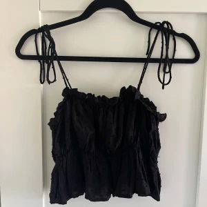 Svart volangig linnetopp från SHEIN - Säljer en svart linnetopp från SHEIN i storlek S. Toppen har tunna axelband som knyts på axlarna och volangiga detaljer. (Kort i storleken)