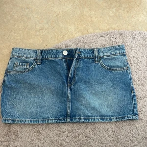 Blå jeanskjol med fickor - Säljer en klassisk blå jeanskjol i kort modell med fram- och bakfickor samt bälteshällor. Kjolen har knapp och dragkedja framtill och är perfekt för en avslappnad stil. Snygg att matcha med en enkel topp<3 storlek 42 men skulle säga att den passar 40 också