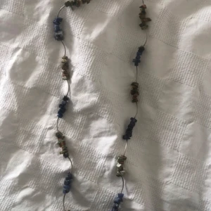 Halsband med blå och gröna stenar - Unikt halsband med oregelbundna blå och gröna stenar på en tunn metalltråd. Stenarna är placerade i grupper längs hela halsbandet och ger en cool, bohemisk vibe. Perfekt för dig som gillar naturliga material och vill sticka ut med accessoarer.