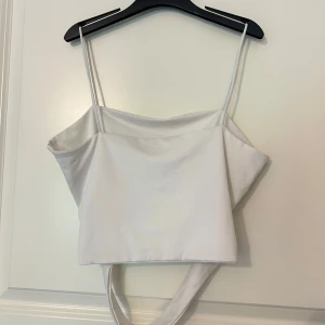 Vit croppad topp från SHEIN - Snygg vit croppad topp från SHEIN med tunna axelband och bred knytning i ryggen. Materialet är mjukt och lätt, vilket gör den skön att bära under exempelvis varma dagar 🌸🌷