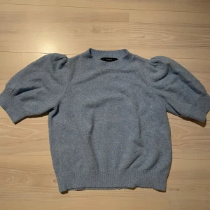 Blå stickad tröja med puffärm Vero Moda - Superfin ljusblå stickad tröja från Vero Moda med puffiga korta ärmar och ribbade muddar. Tröjan har en klassisk rund halsringning och är perfekt för dig som gillar en söt och trendig look. Passar till både jeans och kjol.