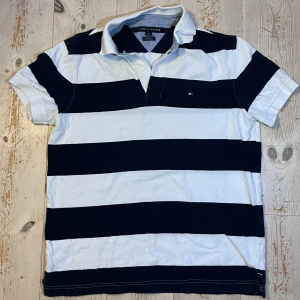 Randig pikétröja Tommy Hilfiger - Snygg pikétröja från Tommy Hilfiger i Custom fit-modell med breda ränder i marinblått och vitt. Klassisk krage, korta ärmar och liten logga på bröstet. Nypris 1100kr. Pris kan diskuteras vid snabb affär.