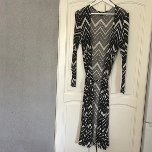 Svartvit mönstrad klänning Lindex M - Svartvit långärmad klänning från Lindex i storlek M. Klänningen har ett grafiskt zigzag-mönster, markerad midja med knytband och rund halsringning. Mjuk och stretchig känsla, perfekt för dig som gillar att sticka ut med mönster. Använd ett fåtal ggr.