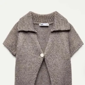 Beige stickad kofta från Zara - Kortärmad stickad kofta från Zara i beige nyans. Koftan har en bred krage och en knapp framtill. Säljer då dom är för korta.