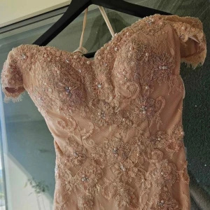 Champagnefärgad spetsklänning med pärlor - Superfin champagnefärgad klänning med blommig spets och pärlbroderier. Offshoulder-modell med figurnära passform och lång längd. Perfekt för dig som vill sticka ut med eleganta detaljer och romantisk vibe perfekt för fest, bröllop. Köpte klänning för 8900kr.