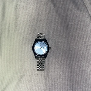 Silverfärgad klocka  - Stilren klocka från Bell & Ross med silverfärgat armband i metall och ljusblå urtavla. Klockan har arabiska siffror, datumvisning och klassisk länkdesign. Perfekt accessoar för dig som gillar en clean och modern look.