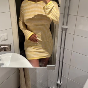 Randig miniklänning  - Miniklänning i gula och vita ränder och lång ärm. Klänningen har en figurnära passform och är tillverkad i ett stretchigt, mjukt material. 💛
