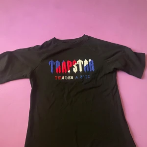 Svart Trapstar t-shirt  - Svart t-shirt från Trapstar med broderad logga i blått, rött och vitt på bröstet. Klassisk passform med korta ärmar och rund hals. Materialet är mjuk bomull som känns skönt mot huden. Perfekt för dig som gillar streetwear.