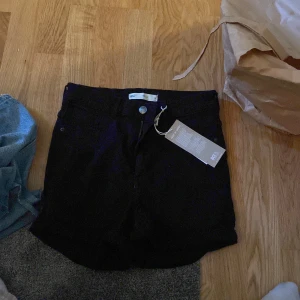 Svarta jeansshorts från Gina Tricot - Snygga svarta jeansshorts från Gina Tricot, modell Molly. De är högmidjade med klassisk femficksdesign, knapp och dragkedja framtill samt stora bakfickor. Perfekta för en trendig och avslappnad look under sommaren. Har inte använt nån gång och har lappen kvar