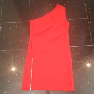 Röd one shoulder kortklänning - Snygg röd kortklänning med one shoulder-design och silvrig dragkedja längs sidan. Klänningen är tight och har en cool asymmetrisk skärning. Perfekt för dig som vill sticka ut med en färgstark look. PRIS KAN DISKUTERAS!