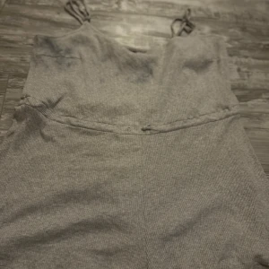 Grå ribbad kortklänning från Divided - Supersöt grå ribbad kortklänning från Divided med smala axelband och enkel, rak passform. Klänningen har en diskret knäppning i midjan och är perfekt för en chill och avslappnad look. Materialet är mjukt och stretchigt för extra komfort.