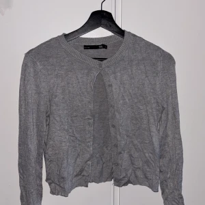 Grå kofta från lager 157, XS - En enkel och stilren grå kofta från lager 157 i storlek XS. Koftan har rund halsringning, långa ärmar och knäppning framtill