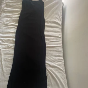 Svart långklänning från Nelly - Enkel och stilren svart långklänning från Nelly med smala axelband och rak passform. Perfekt för dig som gillar minimalistisk stil och vill ha en klänning som känns både bekväm och snygg. Materialet är mjukt och följsamt. Kan vara lite nopprig. Stretchig så passar en M oxå dock så är den normla i storlek