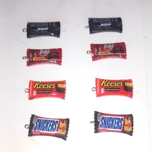 Chokladgodis örhängen mix - Säljer coola örhängen formade som klassiska chokladgodisar: Hershey's, KitKat, Reese's och Snickers. Färgglada och detaljerade i svart, rött, orange och brunt. Perfekt accessoar för dig som älskar godis och vill sticka ut med något unikt!