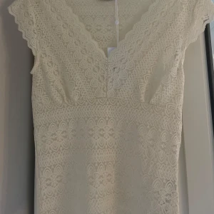 Vit spetstopp från Vila - Superfin vit spetstopp från Vila med v-ringning och korta ärmar. Toppen har ett vackert blommigt spetsmönster och är figurnära med kort längd. Den är helt oanvänd och har prislappen kvar på tröjan. Säljer då den vart lite för stor för mig. Storlek M