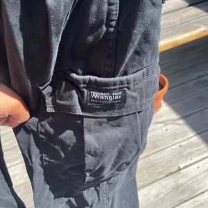 Svarta cargobyxor från Wrangler - Svarta cargobyxor från Wrangler Urban Outfitters. Byxorna har flera praktiska fickor, raka ben och klassisk cargostil. Perfekta för dig som gillar en avslappnad look med funktionella detaljer.