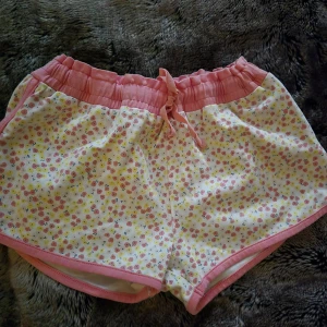 Blommiga shorts från Polarn O. Pyret - Söta shorts från Polarn O. Pyret i storlek 134/140. De är vita med små blommor i rosa och gult, har rosa midja med snörning och rosa kant längs benen. Perfekta för varma sommardagar och superbekväma tack vare mjukt bomullsmaterial.