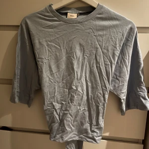 Ljusblå topp med öppen rygg  - Säljer denna snygga t-shirt med knytning från Nelly! Helt oanvänd med lappen kvar! Den är skrynklig då den legat i min byrå, försvinner om man stryker den🩵🩵färgen finns inte längre vilket gör den exklusiv och perfekt för en trendig look! Skriv vid intresse 