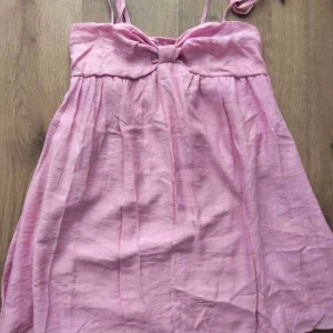 Rosa kort sommarklänning med rosett - Söt rosa kortklänning med smala axelband och en fin rosettdetalj framtill. Perfekt till när de är varmt ute!!